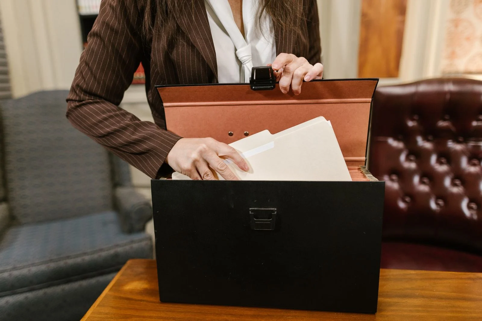 A businesswoman sorts paper files from a black box at an office desk.