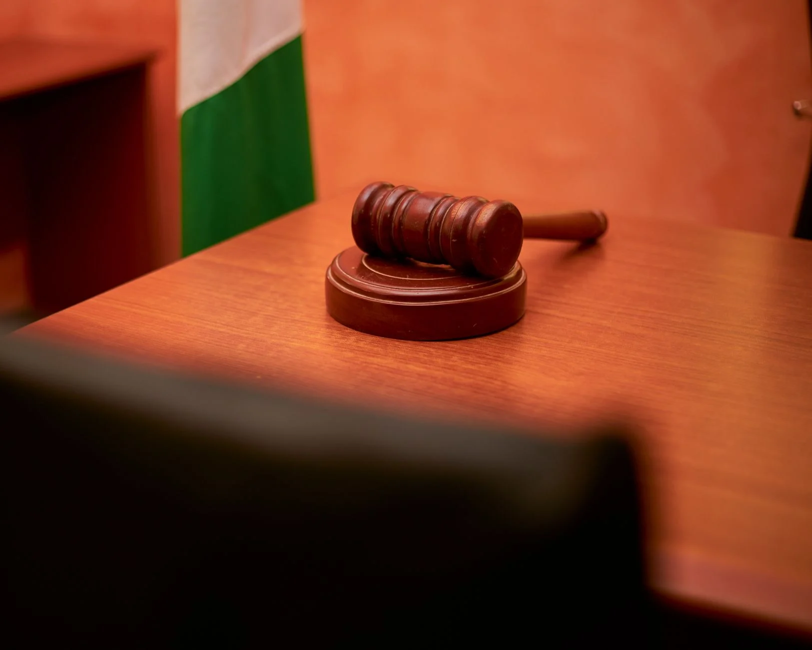 A close-up of a wooden gavel resting on a courtroom desk.