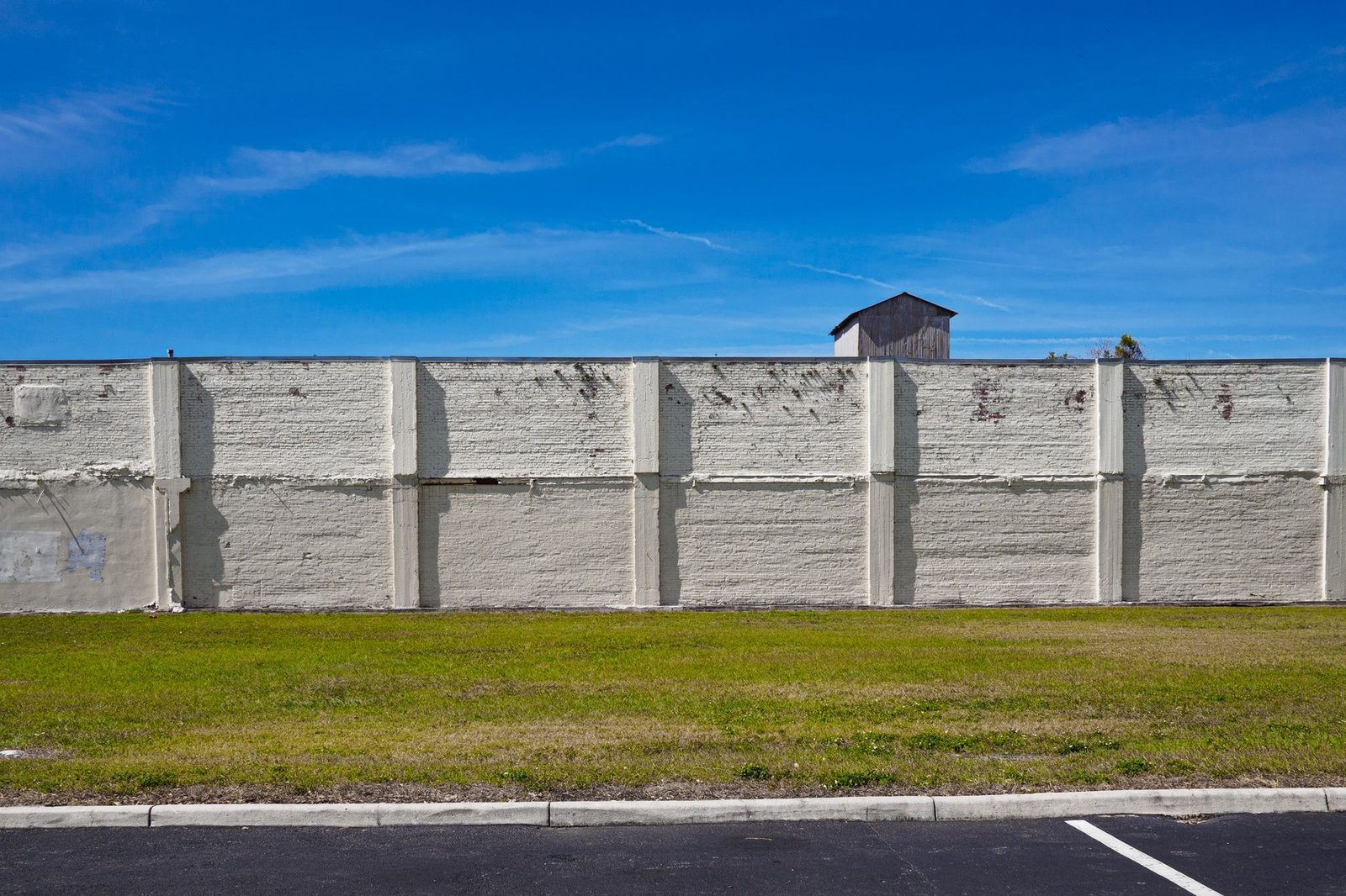 A concrete wall beneath a clear blue sky, with green grass growing in an urban setting.