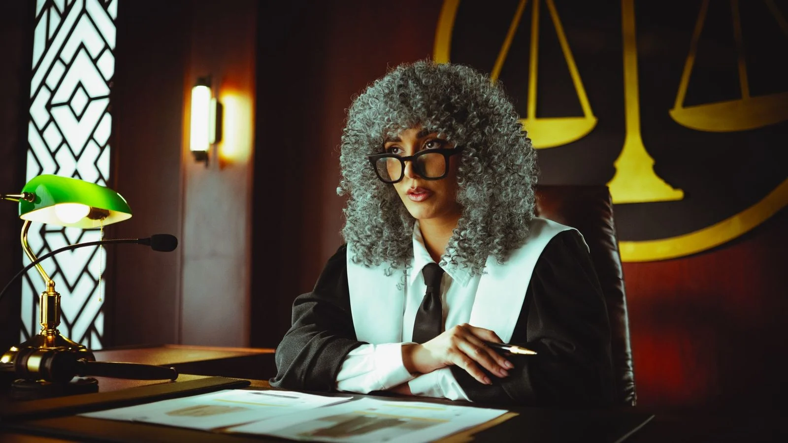 Una jueza sentada en su escritorio en una sala de tribunal, con una balanza de la justicia visible al fondo.
