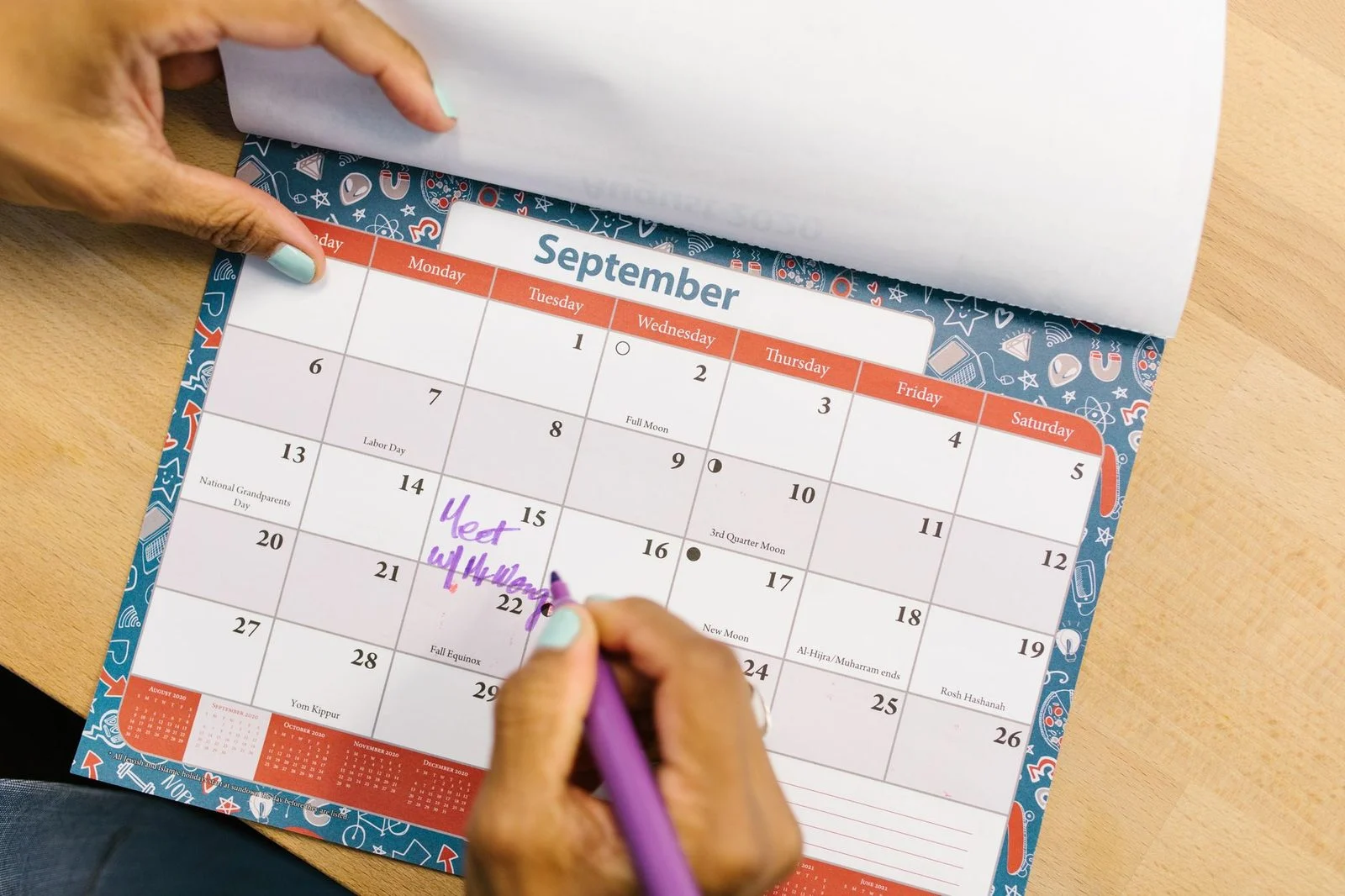 Persona marcando una fecha en un calendario con bolígrafo morado sobre un escritorio de madera.
