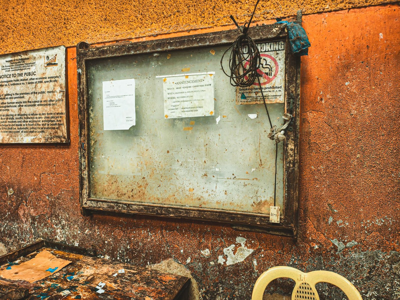 A rustic notice board with announcements pinned to a textured orange wall.