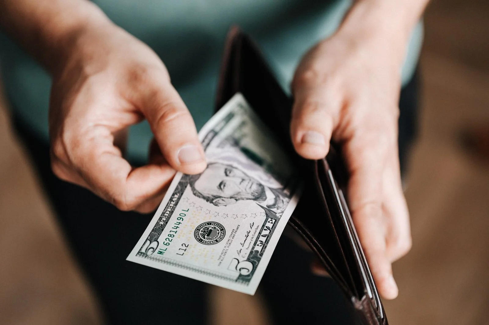 Close-up of a man in casual clothes pulling dollar bills from his wallet to pay at a shop.