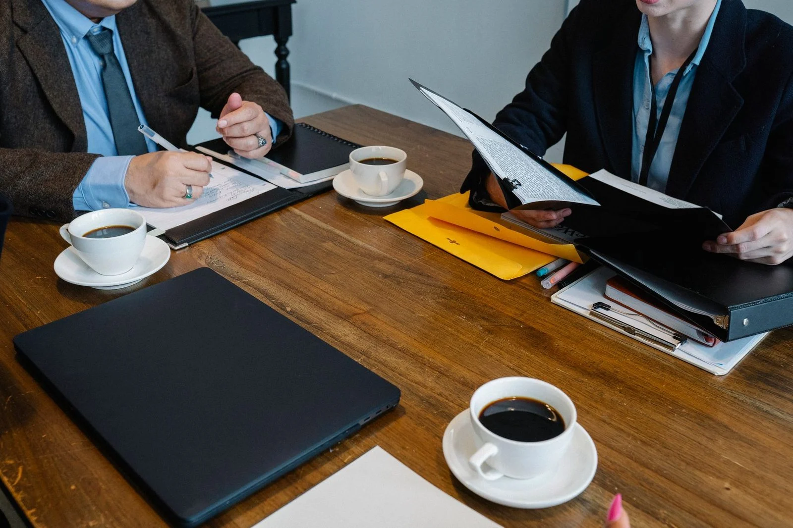 Coworkers in formal clothes review documents and drink coffee at a table.
