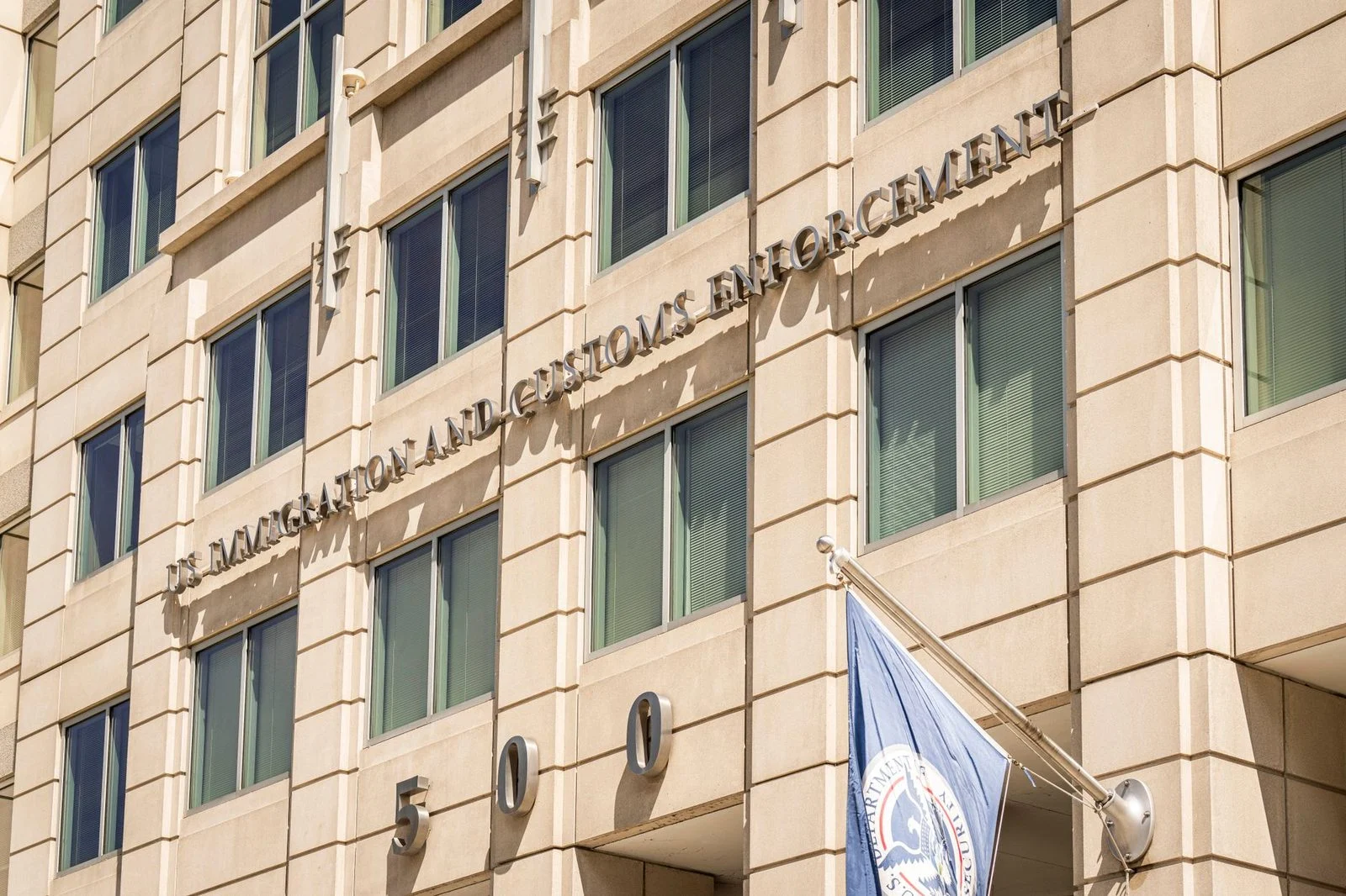 Exterior view of a U.S. Immigration and Customs Enforcement building with a flag and signage.