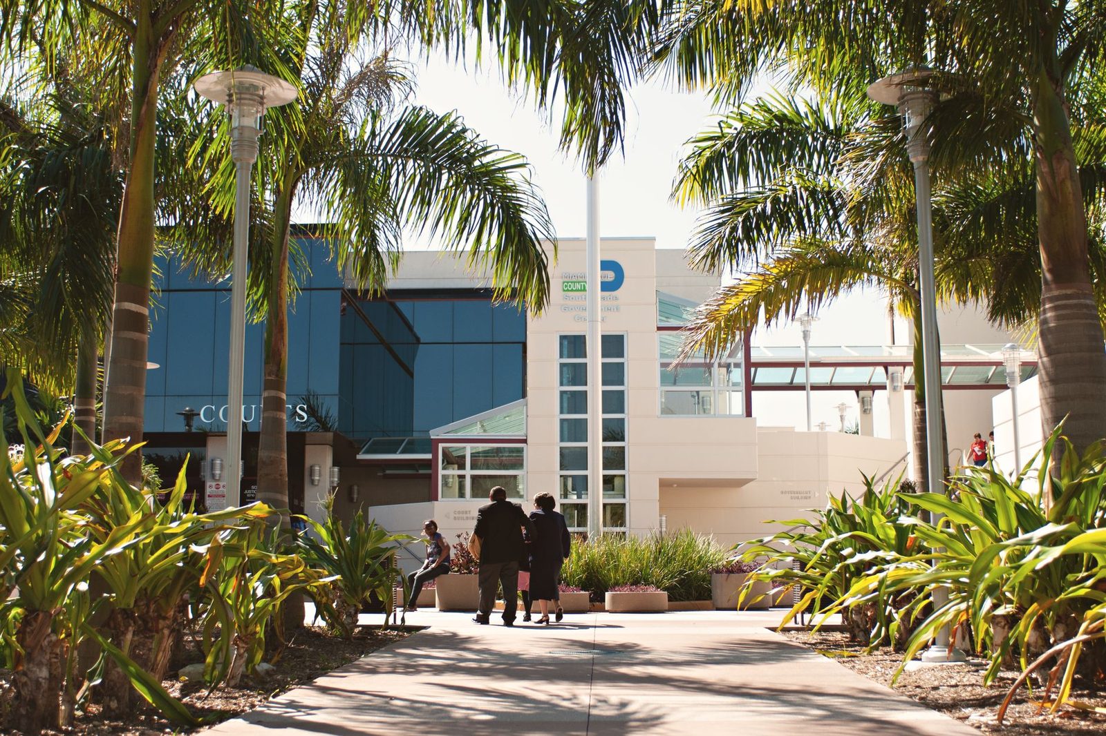 Miami courthouse with palm trees and people under a bright sunny sky.
