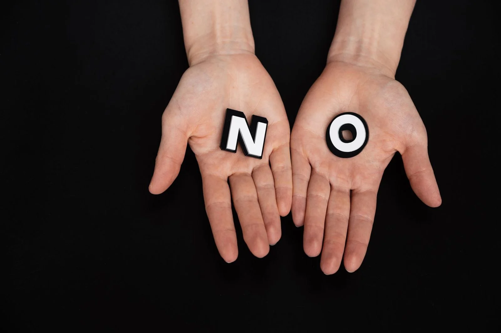 Open palms cradle wooden letters spelling "NO" against a black background.
