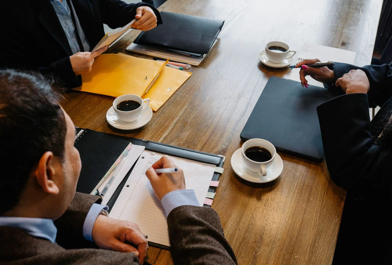 Overhead view of diverse coworkers seated at a table with documents and coffee, discussing business.