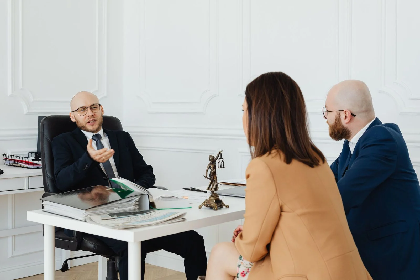 Three adults in business attire meet at a conference table in an office to discuss legal matters.