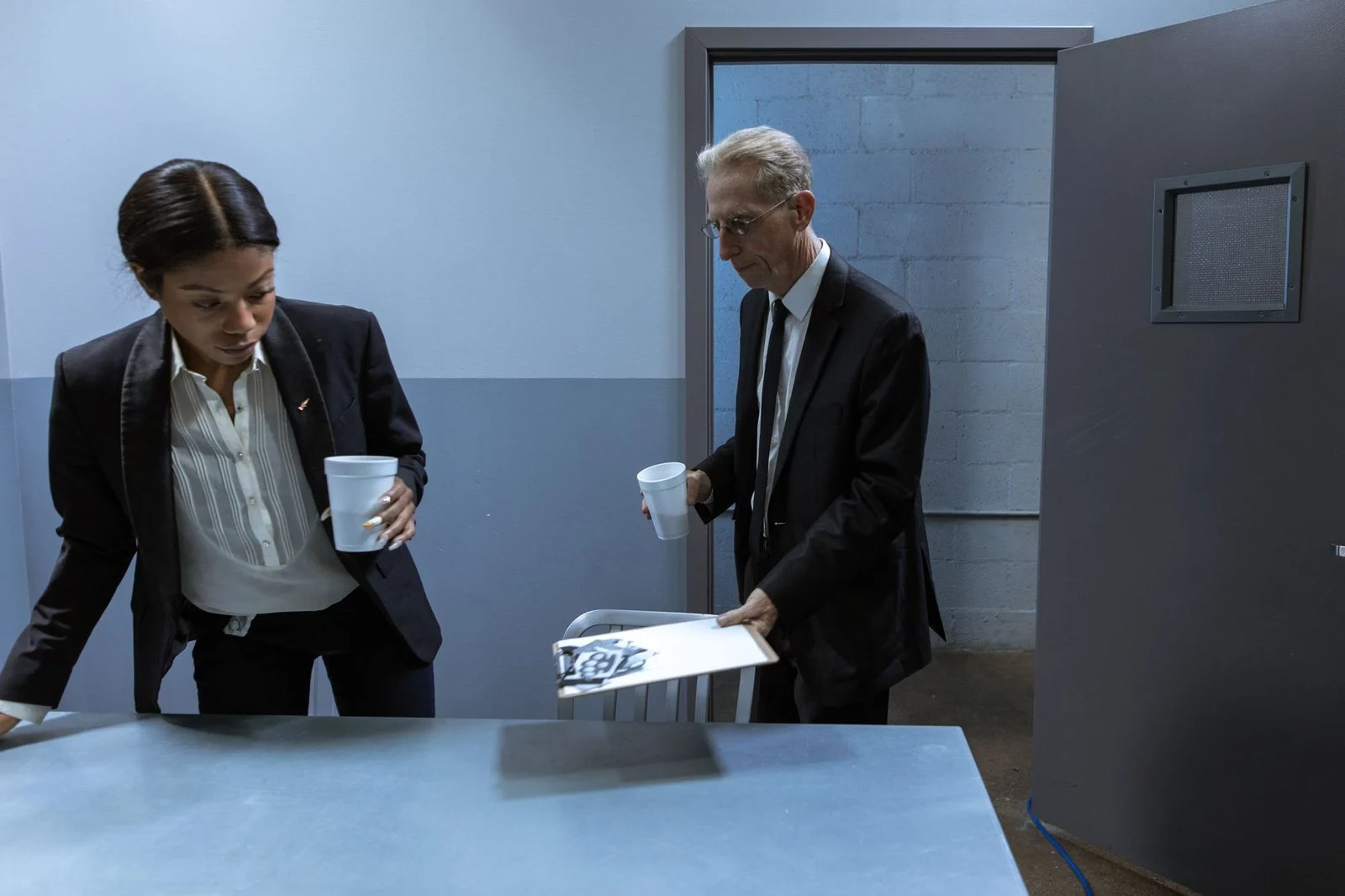 Two professionals sit at a table in an office, reviewing confidential documents together over coffee.
