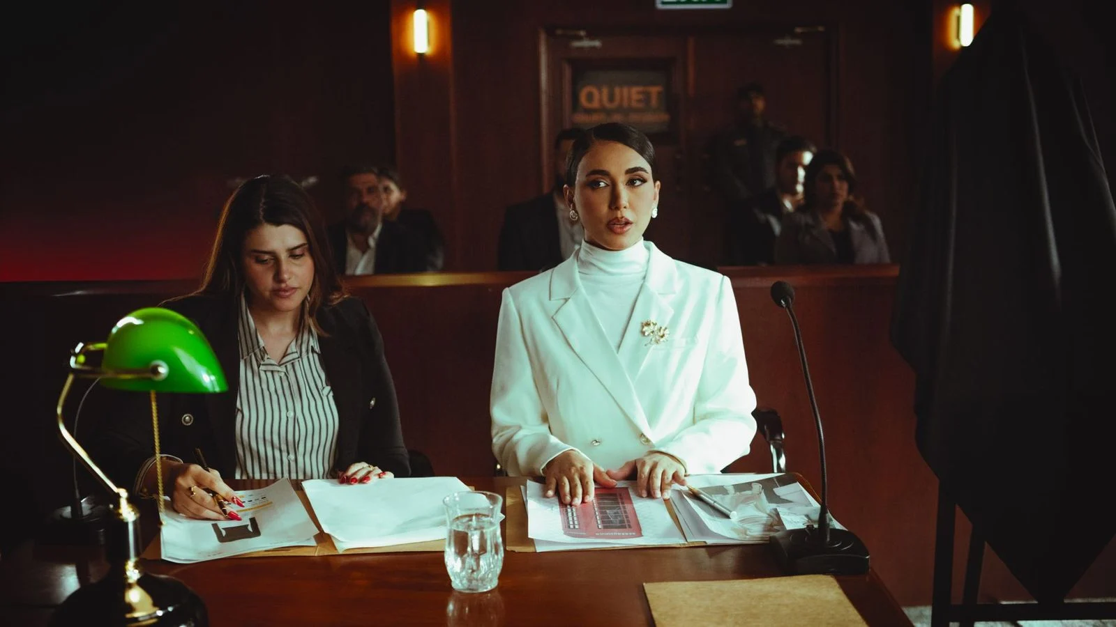 Dos mujeres con ropa de oficina revisan documentos legales juntas en una mesa de tribunal.