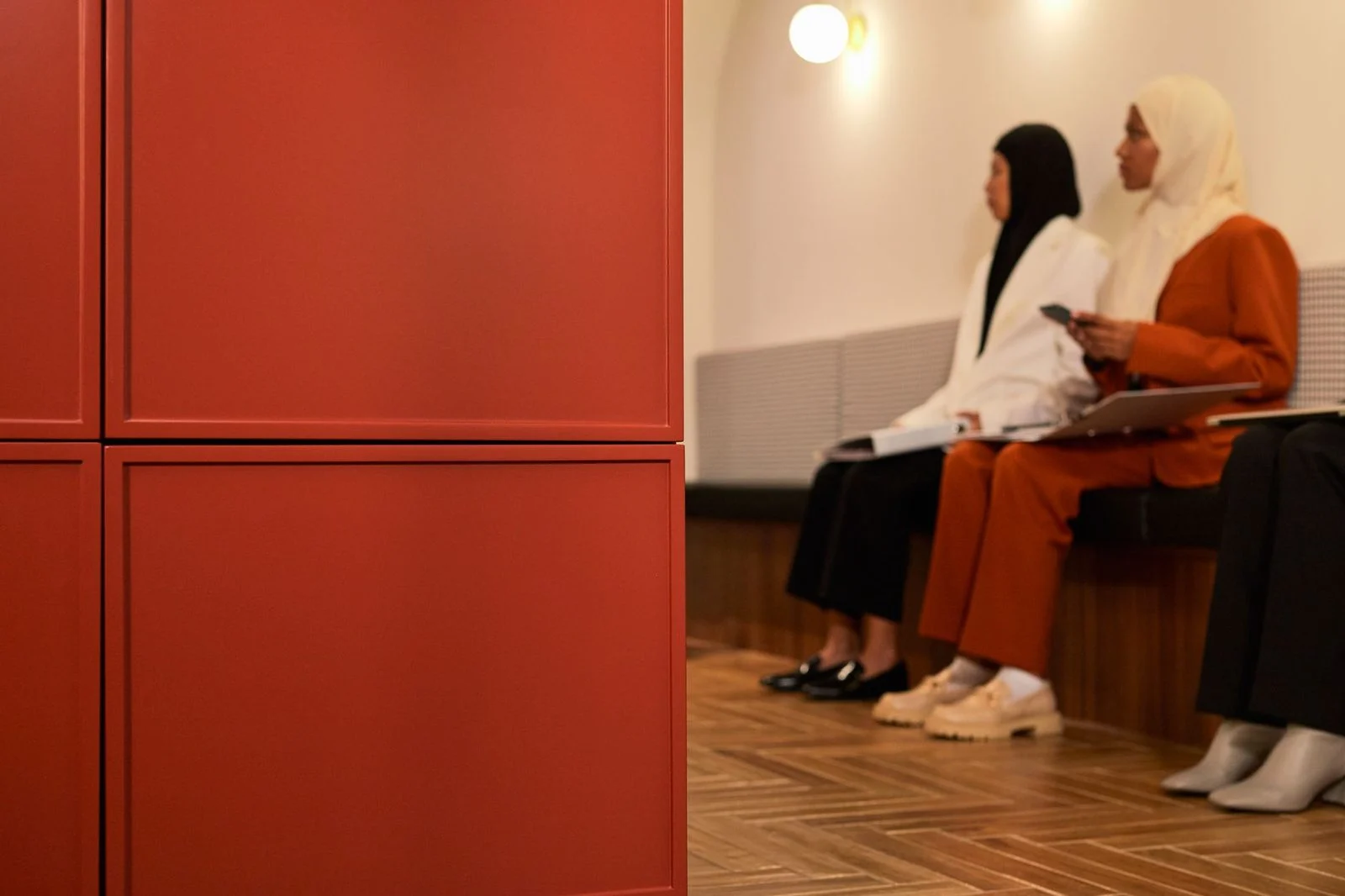 Modern office waiting room with several women seated near a red wall panel.