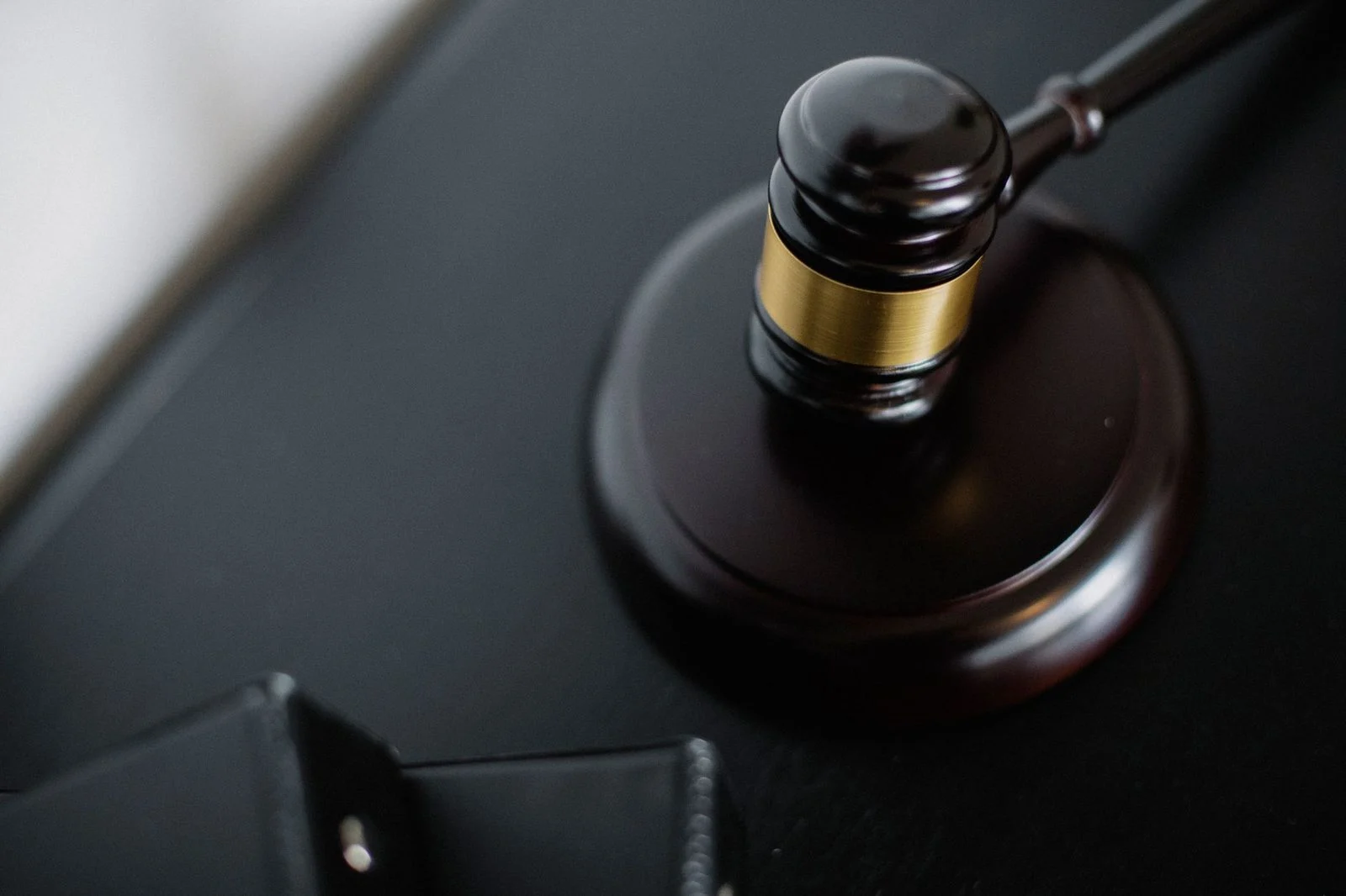 Un mazo de madera sobre una superficie redonda junto a carpetas sobre una mesa en una sala de tribunal, fotografiado desde arriba.